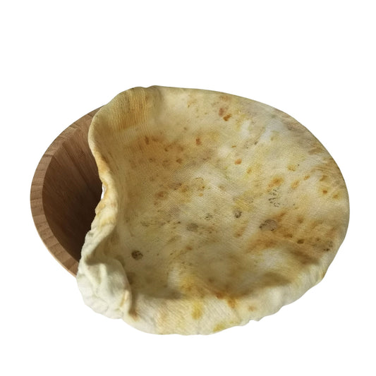 Charlotte couvre-plat en lin ancien, teinte naturellement avec des pigments végétaux issus de pelures d’oignon jaune, de fleurs de pissenlit et de jeunes feuilles d’eucalyptus. Le tissu présente un effet moucheté jaune et beige avec des nuances organiques, recouvrant un saladier en bois. Accessoire réutilisable et écologique pour la cuisine zéro déchet.