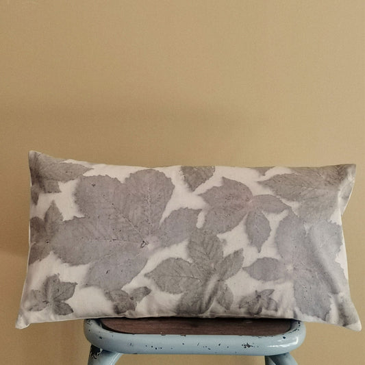 Coussin rectangulaire 30x50 cm en toile de coton ancienne teint à la main avec des feuilles de marronnier, posé sur un tabouret vintage.