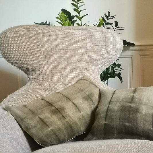 Duo de coussins en lin ancien, teints naturellement au mimosa avec un effet tie and dye subtil, présenté sur un fond neutre. Teintes douces sable et vert kaki, finition artisanale.