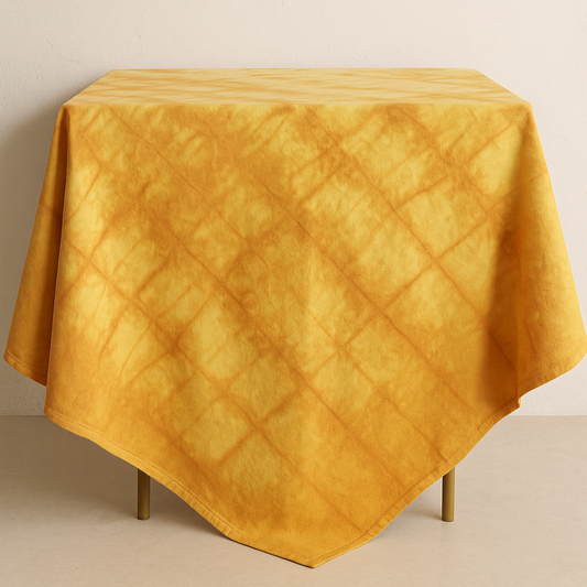 Table de jardin en Provence avec nappe carrée jaune doré en linge ancien, teinte naturellement à la main avec des pelures d’oignons. Ambiance bohème et estivale.
